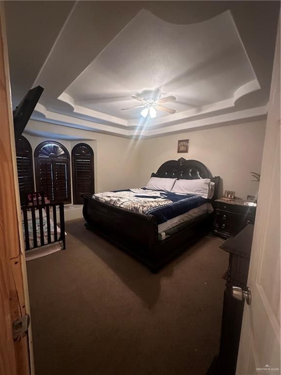 carpeted bedroom featuring a raised ceiling and ceiling fan