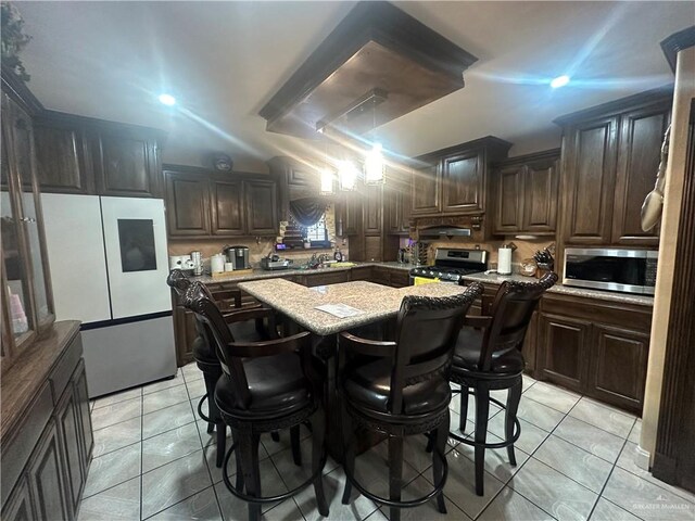 kitchen with a center island, stainless steel appliances, light stone counters, and dark brown cabinetry