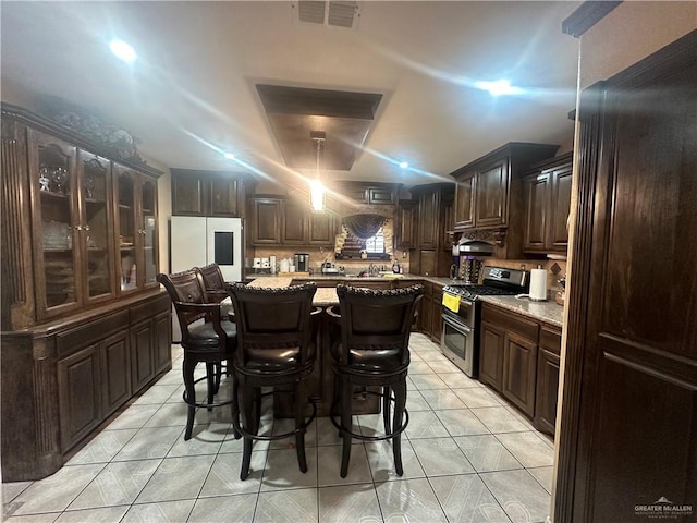 kitchen with dark brown cabinets, a center island, stainless steel gas stove, white fridge, and light tile patterned flooring