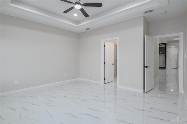 spare room with marble finish floor, visible vents, a tray ceiling, and baseboards