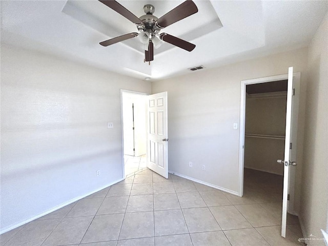 unfurnished bedroom featuring light tile patterned floors, a walk in closet, a closet, and ceiling fan