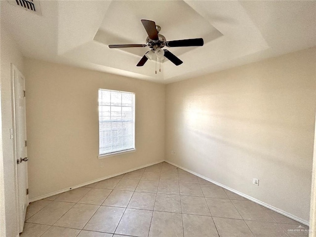 empty room with light tile patterned floors, a tray ceiling, and ceiling fan