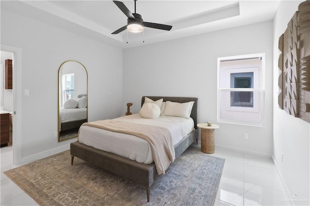 bedroom featuring light tile patterned floors, a tray ceiling, baseboards, and a ceiling fan