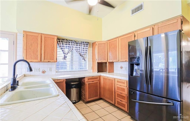 kitchen with tile counters, stainless steel fridge, sink, and a high ceiling