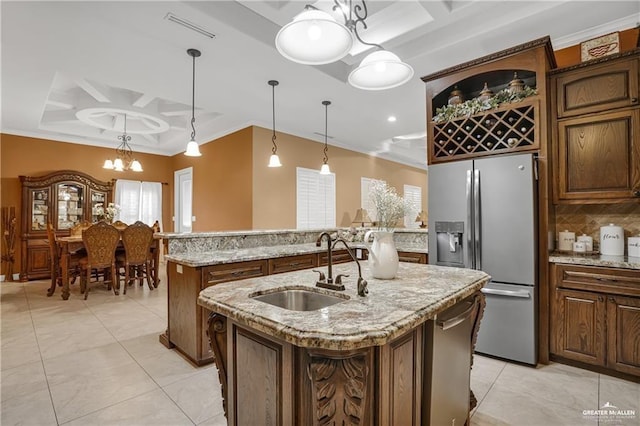 kitchen with sink, hanging light fixtures, light stone counters, stainless steel refrigerator with ice dispenser, and a center island with sink