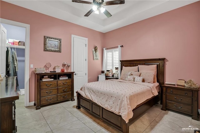 bedroom with a raised ceiling, a walk in closet, ceiling fan, and a closet