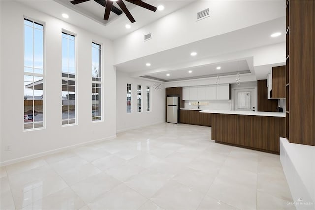 kitchen with a tray ceiling, stainless steel refrigerator, sink, ceiling fan, and kitchen peninsula