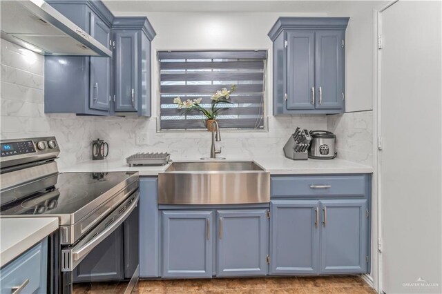 kitchen with sink, wall chimney exhaust hood, decorative backsplash, stainless steel electric range oven, and blue cabinetry