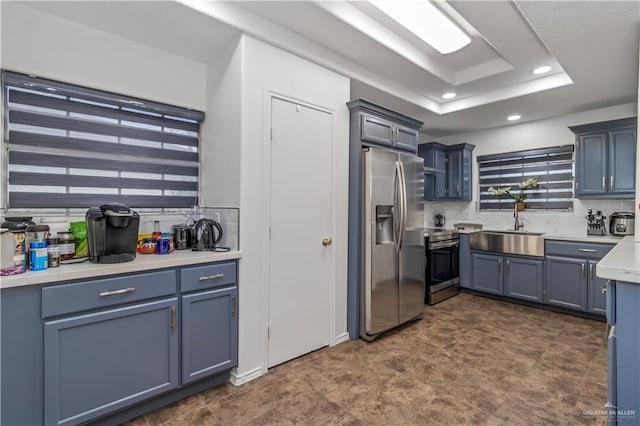 kitchen with decorative backsplash, appliances with stainless steel finishes, a raised ceiling, sink, and blue cabinetry