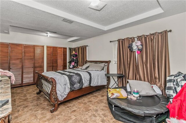 bedroom with a raised ceiling, two closets, and a textured ceiling