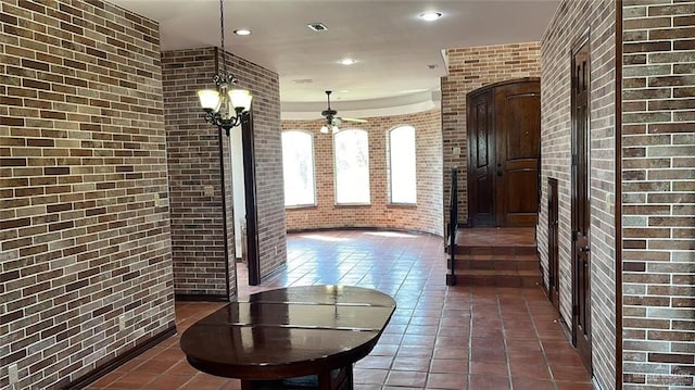 hall with brick wall, dark tile patterned flooring, and an inviting chandelier