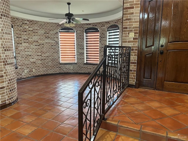 foyer with tile patterned flooring, ceiling fan, and brick wall