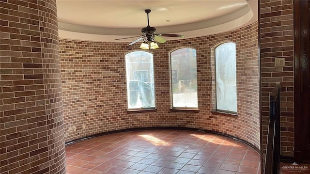 unfurnished room featuring tile patterned floors, ceiling fan, and brick wall