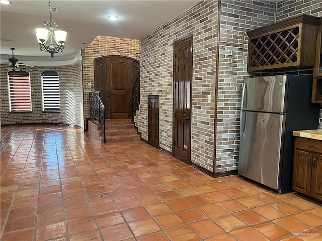 kitchen with stainless steel fridge, decorative light fixtures, and brick wall