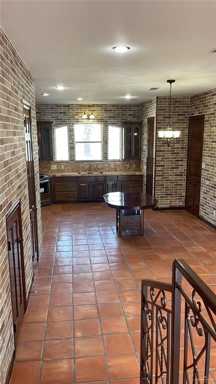 kitchen featuring brick wall, dark brown cabinetry, sink, decorative light fixtures, and an inviting chandelier