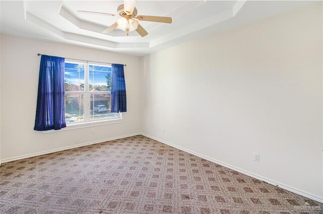 carpeted spare room featuring a raised ceiling and ceiling fan