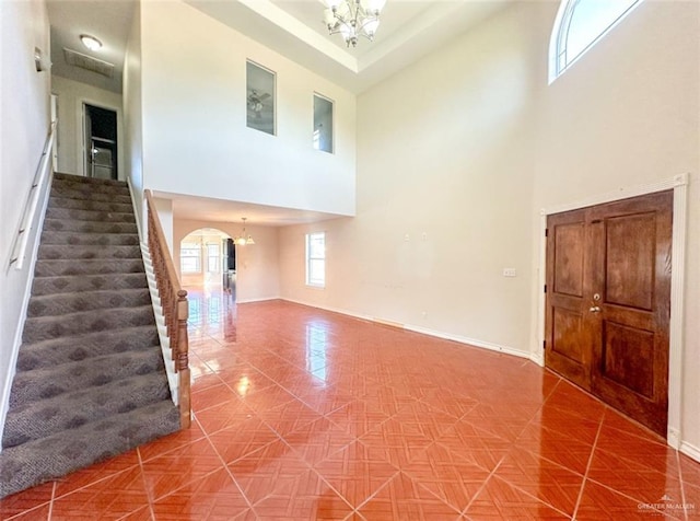 unfurnished living room featuring a towering ceiling, tile patterned floors, and a chandelier