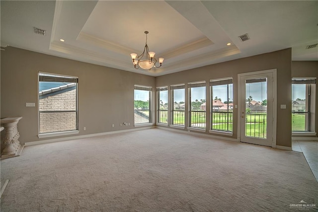 carpeted spare room with a tray ceiling, an inviting chandelier, and plenty of natural light