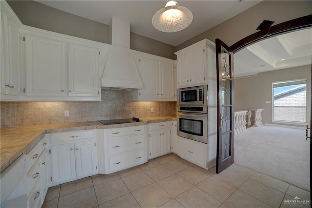 kitchen with tasteful backsplash, stainless steel appliances, light colored carpet, beam ceiling, and white cabinetry