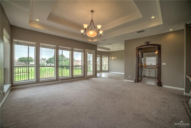 carpeted spare room with ornamental molding, a tray ceiling, and a chandelier