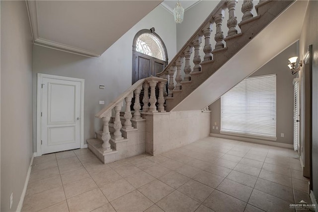 stairway with tile patterned floors, ornamental molding, a high ceiling, and a chandelier