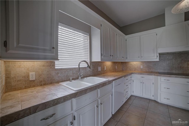 kitchen featuring tasteful backsplash, white dishwasher, sink, white cabinetry, and light tile patterned flooring