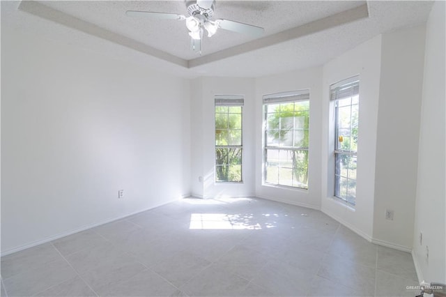 tiled spare room featuring a tray ceiling, ceiling fan, and a textured ceiling