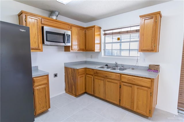 kitchen with light tile patterned flooring, fridge, and sink