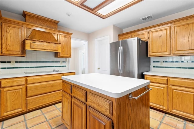 kitchen with a center island, black electric stovetop, visible vents, custom range hood, and freestanding refrigerator