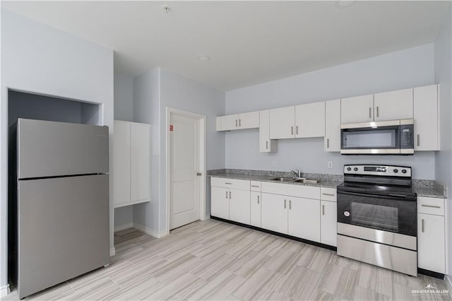 kitchen with light stone counters, white cabinets, appliances with stainless steel finishes, and sink