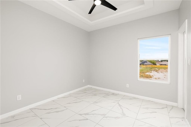 empty room with ceiling fan and a tray ceiling