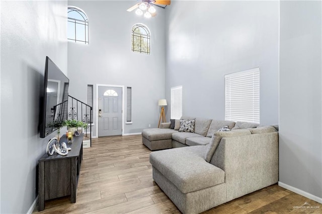 living room with ceiling fan, a towering ceiling, and light wood-type flooring