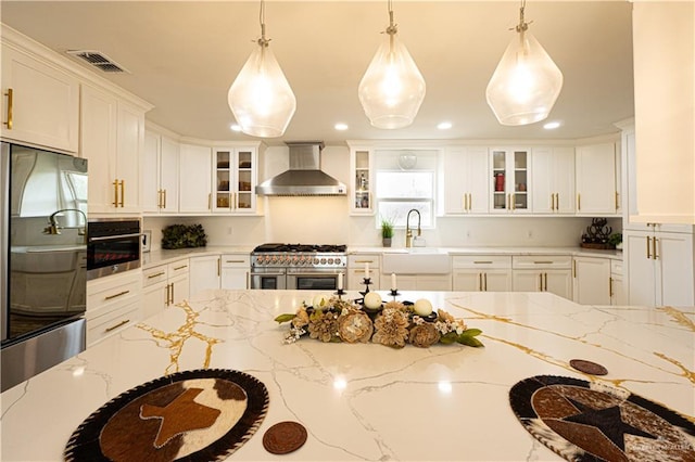 kitchen featuring light stone counters, stainless steel appliances, hanging light fixtures, and wall chimney range hood