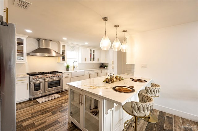 kitchen featuring wall chimney exhaust hood, stainless steel appliances, hanging light fixtures, and white cabinets