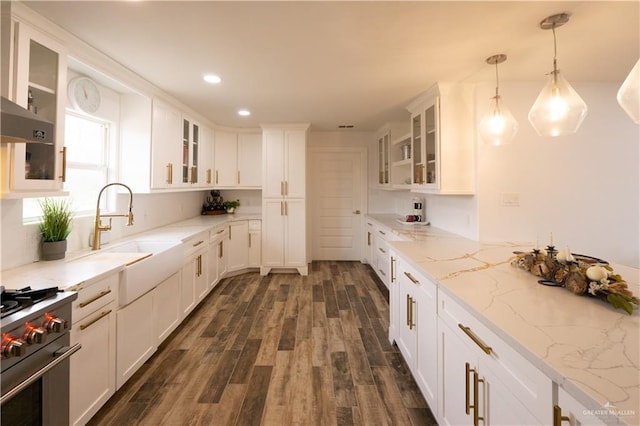 kitchen with sink, high end range, hanging light fixtures, white cabinetry, and light stone counters