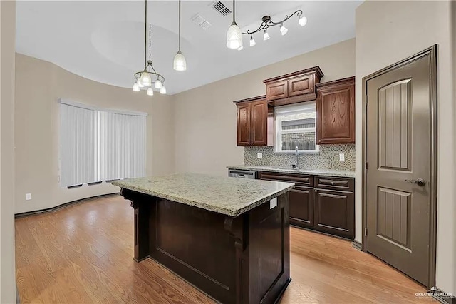 kitchen with a kitchen island, sink, a kitchen breakfast bar, hanging light fixtures, and light hardwood / wood-style floors