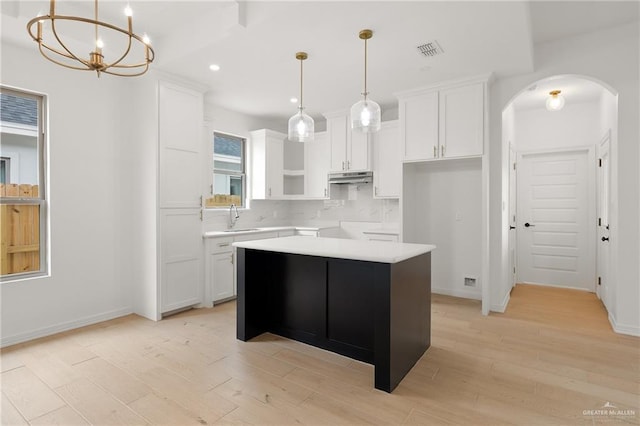 1305 Franklin Ave, Alton, TX 78573 - kitchen with arched walkways, a kitchen island, under cabinet range hood, a sink, and light wood-style floors