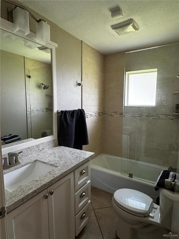 1108 Ash Dr, Weslaco, TX 78596 - full bath with a textured ceiling, toilet, vanity, tile patterned flooring, and  shower combination