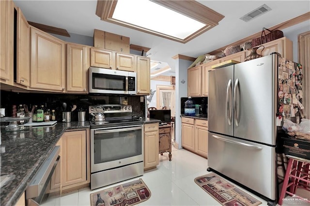 kitchen featuring light brown cabinetry, decorative backsplash, stainless steel appliances, and dark stone counters