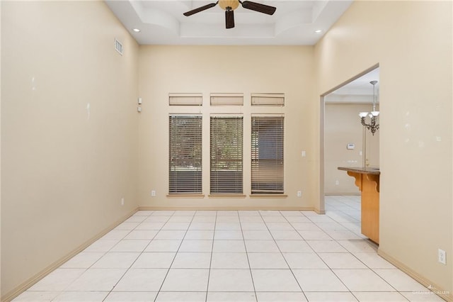 tiled spare room featuring a raised ceiling, a high ceiling, and ceiling fan with notable chandelier