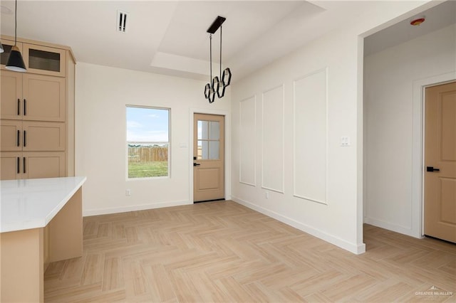 unfurnished dining area with a raised ceiling, light parquet flooring, and a chandelier