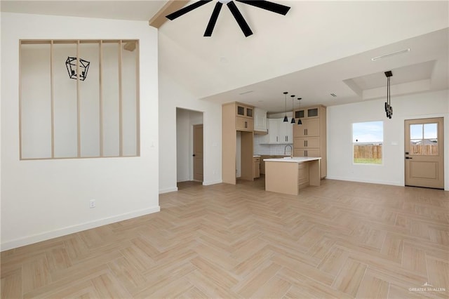 unfurnished living room with sink, a high ceiling, ceiling fan, a tray ceiling, and light parquet flooring