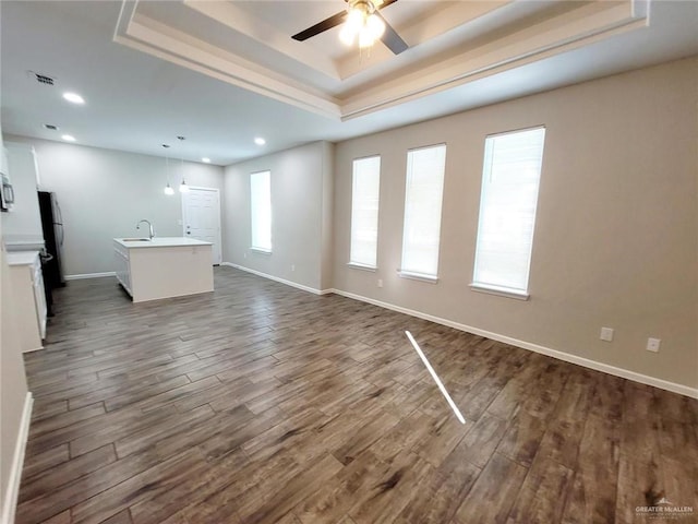 unfurnished living room with ceiling fan, dark hardwood / wood-style floors, a raised ceiling, and sink