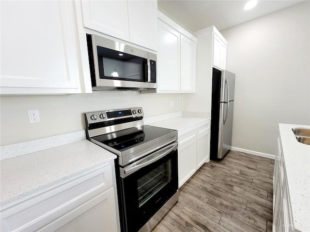 kitchen featuring sink, light hardwood / wood-style flooring, light stone counters, white cabinetry, and stainless steel appliances