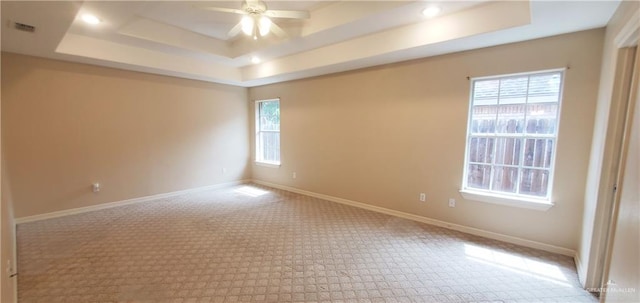 spare room featuring light colored carpet, a raised ceiling, and ceiling fan