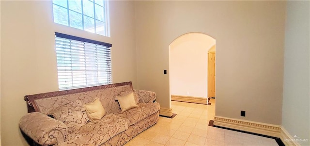 living room featuring light tile patterned floors, a high ceiling, and a baseboard heating unit