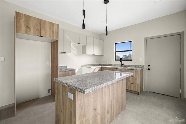 kitchen featuring light stone countertops, a center island, sink, decorative light fixtures, and white cabinets