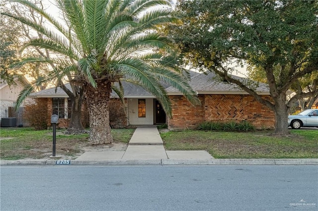 view of front of home featuring a shingled roof, brick siding, and central AC