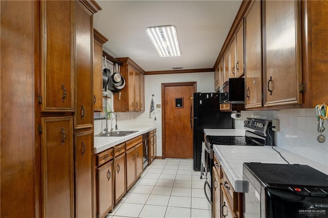 kitchen with brown cabinets, a sink, black appliances, backsplash, and light tile patterned flooring