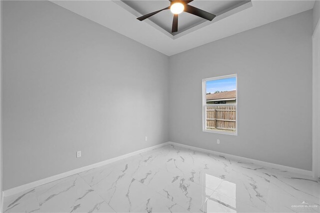 unfurnished room featuring a ceiling fan, a tray ceiling, marble finish floor, and baseboards